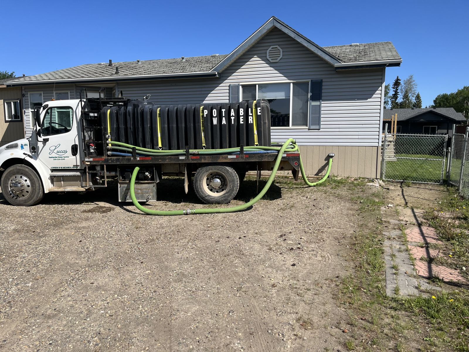 Lucas Water flatbed truck with poly tanks parked at a house, hose run to the cistern
